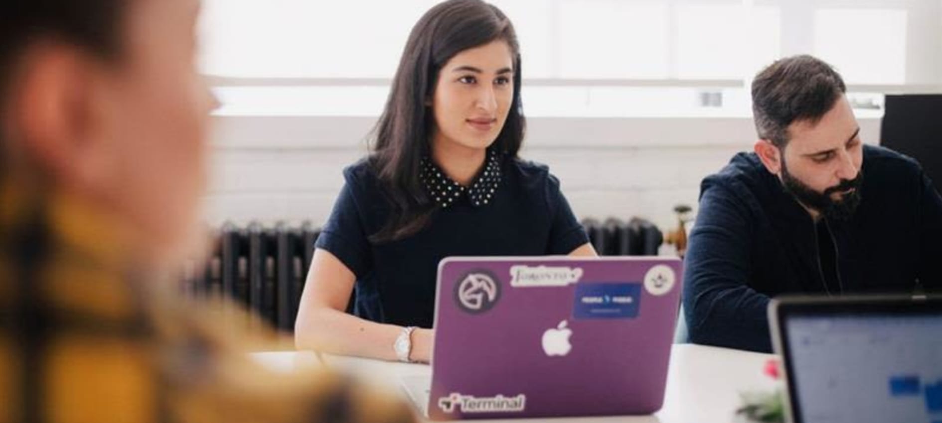 A young woman is in a class room with other students listening intently whilst a laptop is positioned in front of her