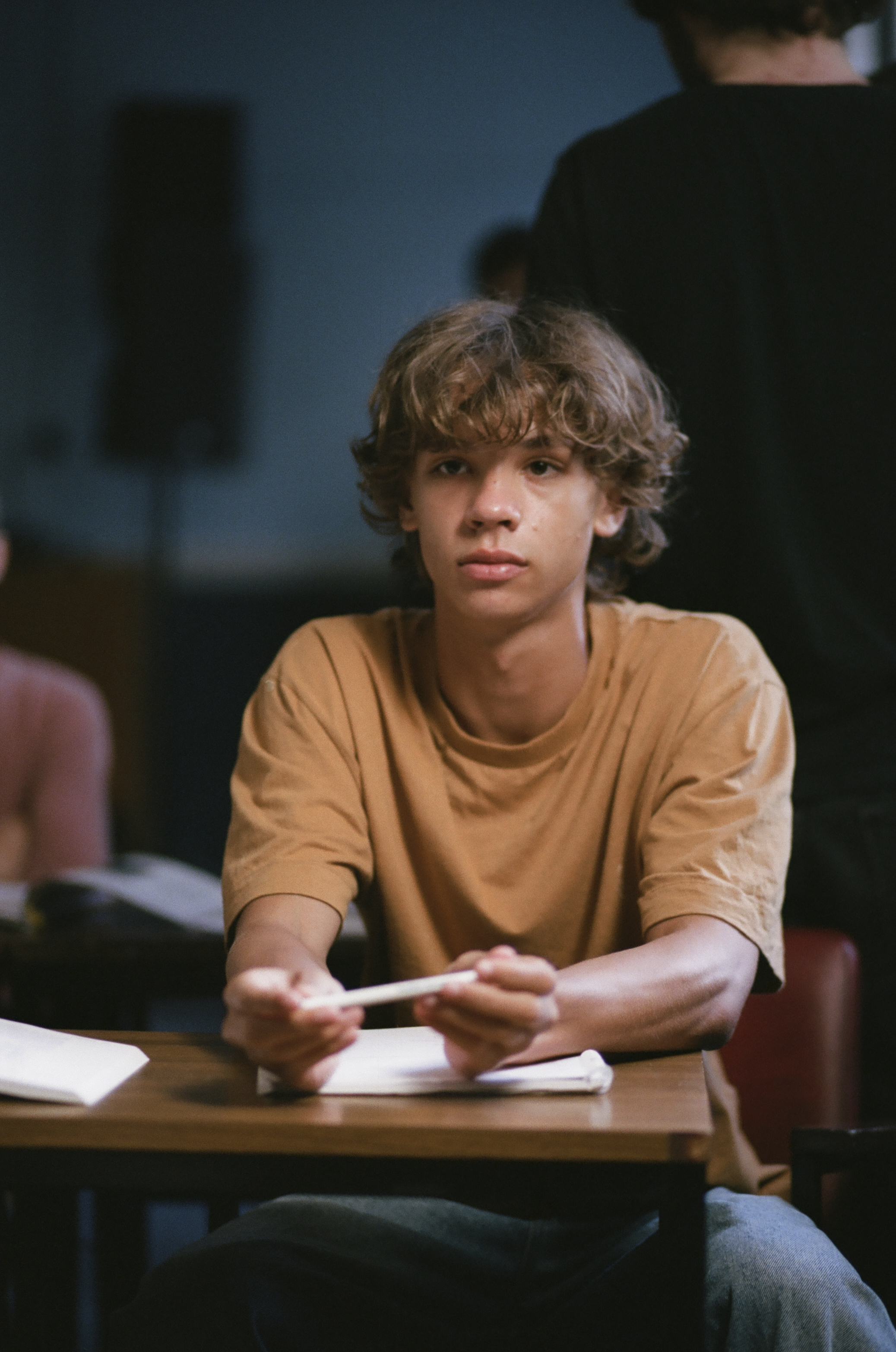 Boy in a classroom sat at a school desk, looking into the distance.