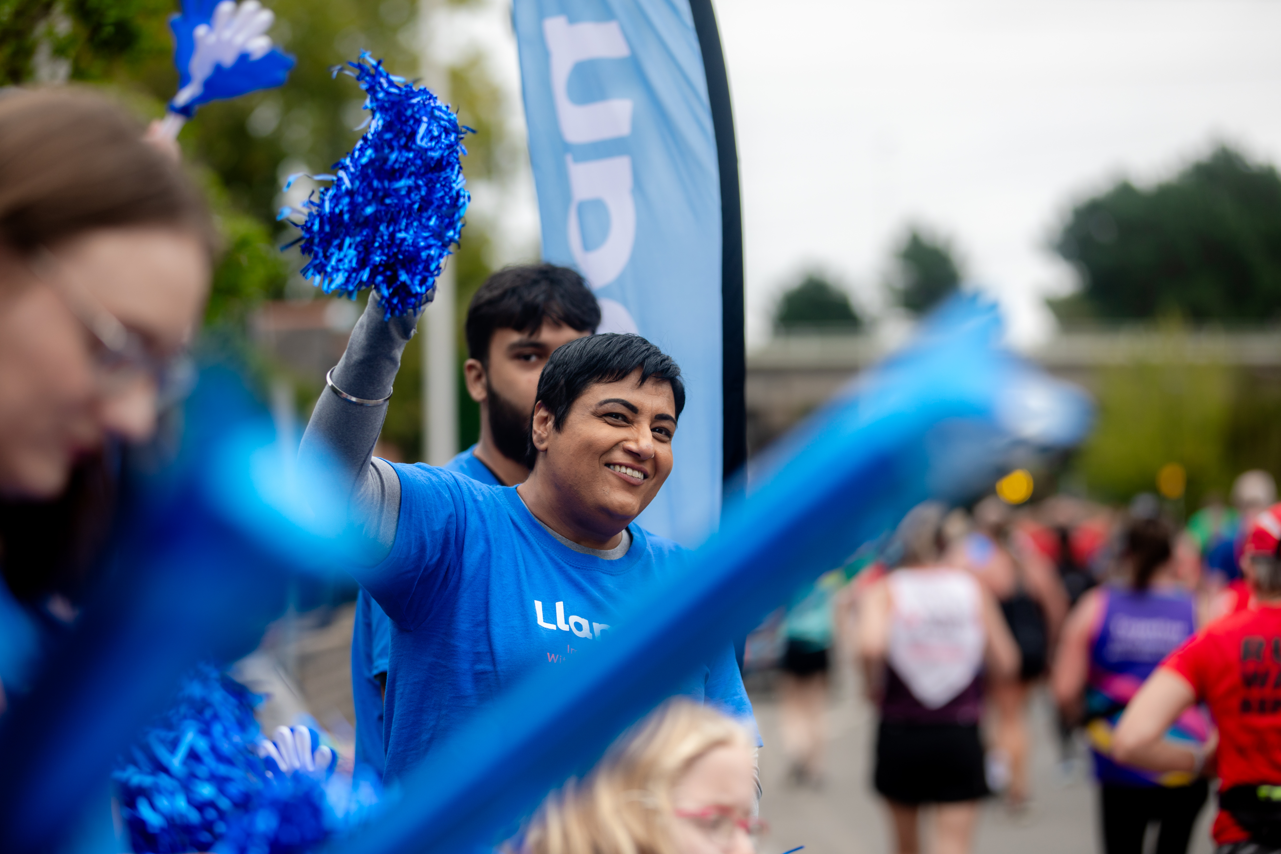 A Llamau staff member wearing a Llamau t-shirt, cheering on fundraisers at the side of a marathon.